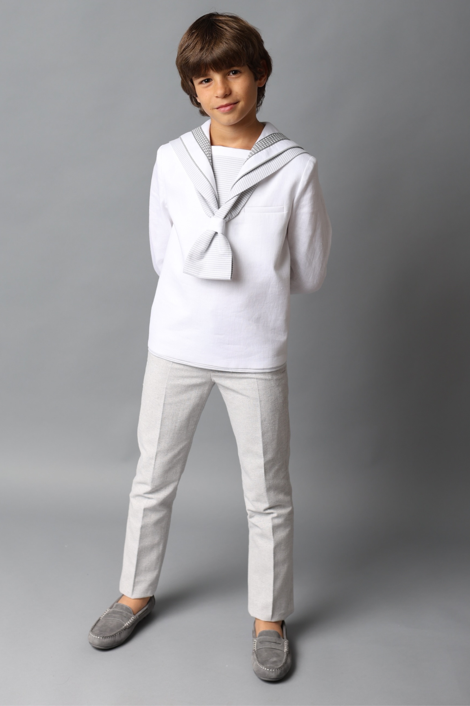 Niño con traje de comunión marinero blanco con detalles en gris, de la colección 2025.