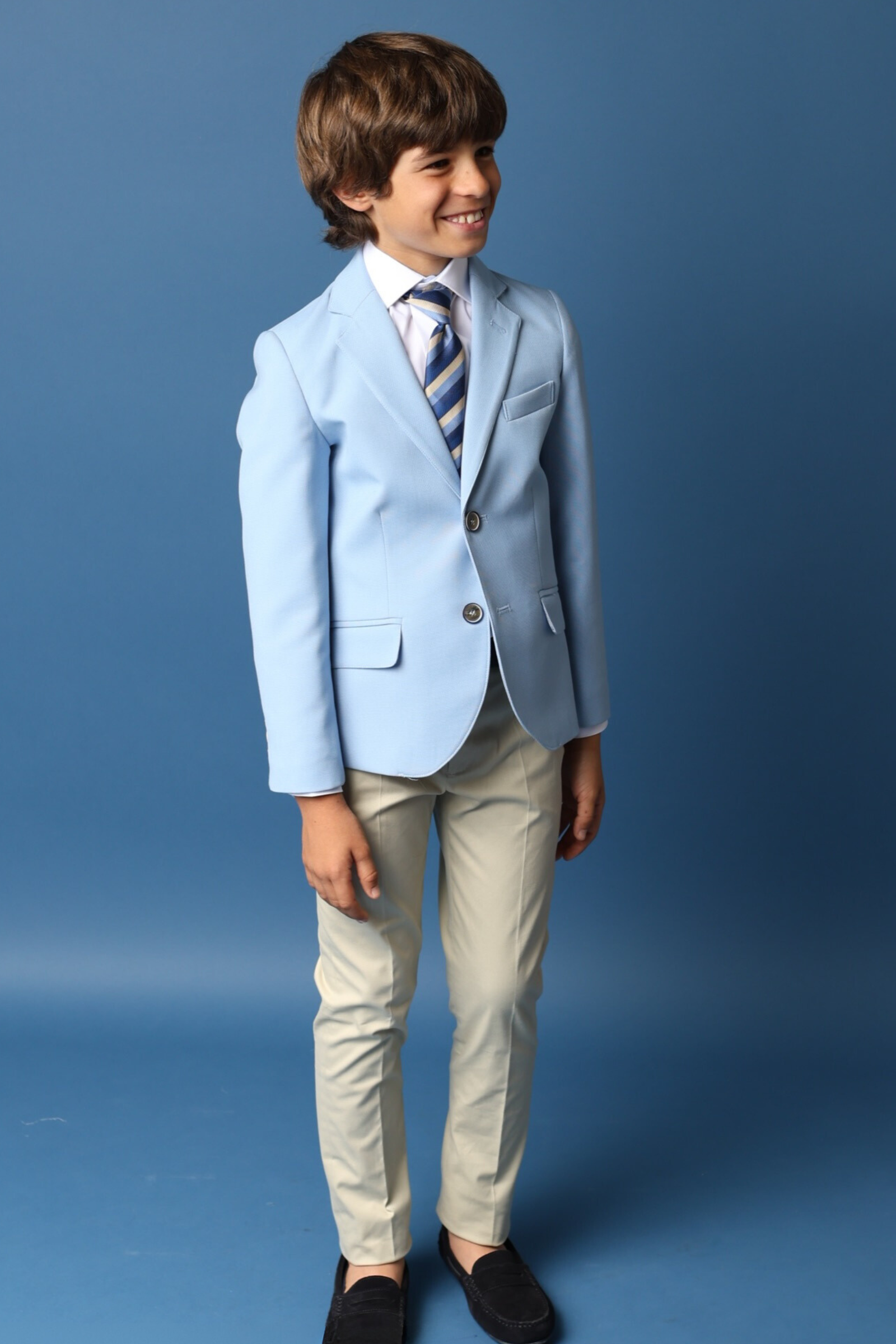 Niño con traje de comunión en azul claro y pantalones beige, perfecto para comuniones 2025.
