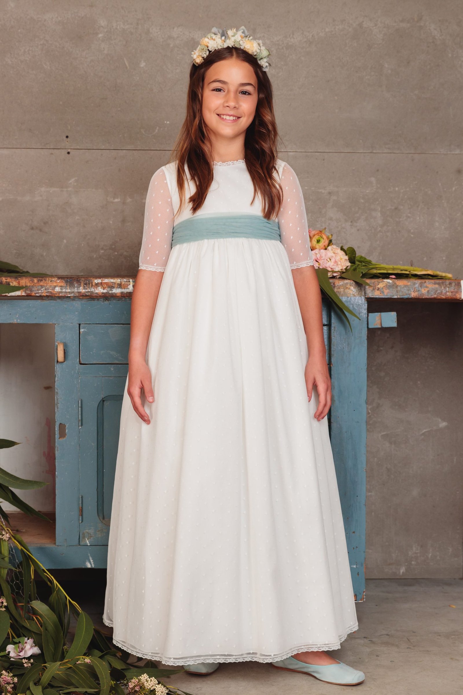 Vestido de comunión niña 2025 blanco con fajín azul cielo, mangas de tul y corona de flores, exclusivo en MartaMolina.com