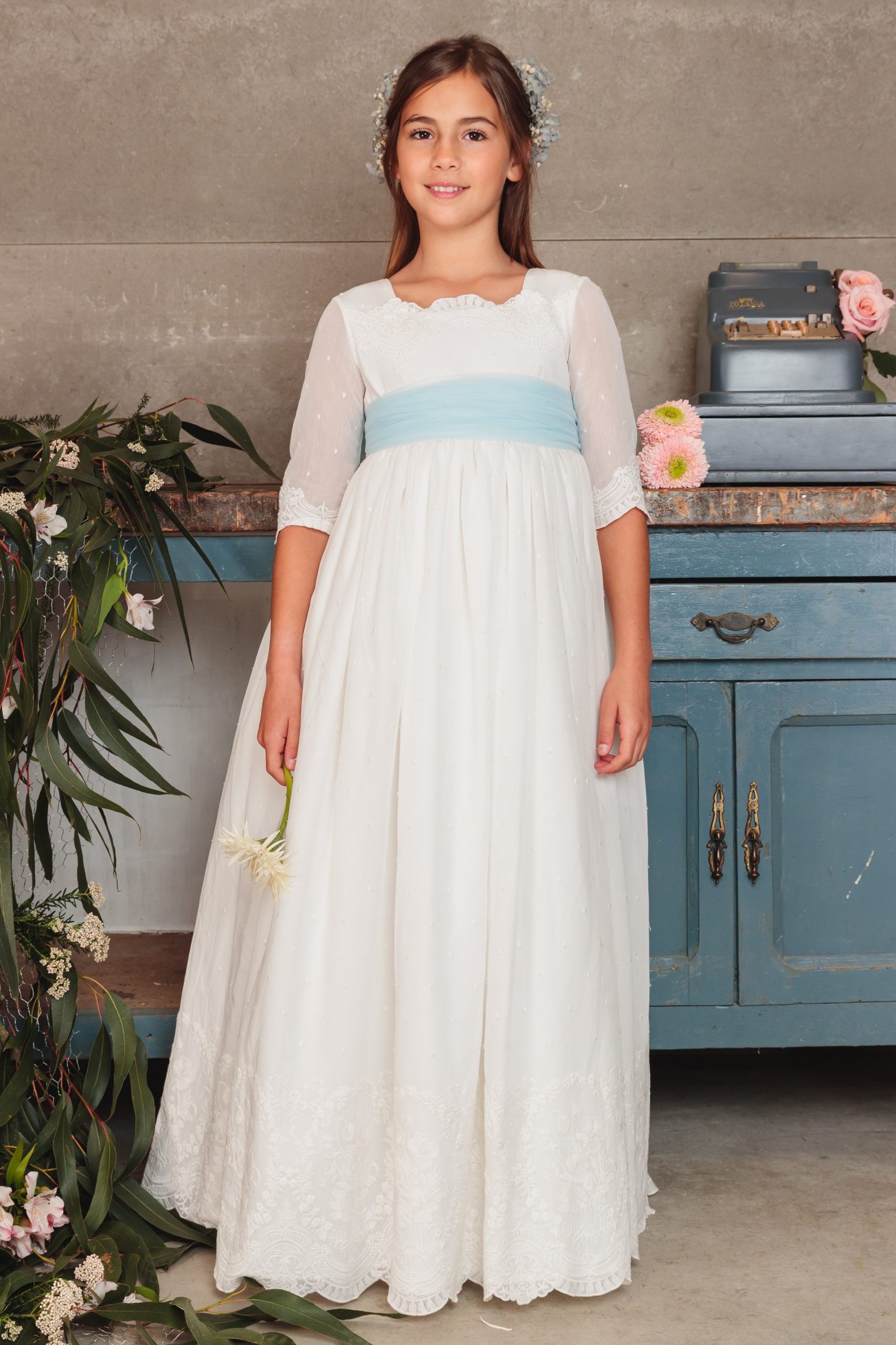 Vestido de comunión niña 2025 blanco con fajín celeste, mangas tres cuartos de tul y tocado floral, exclusivo en MartaMolina.com
