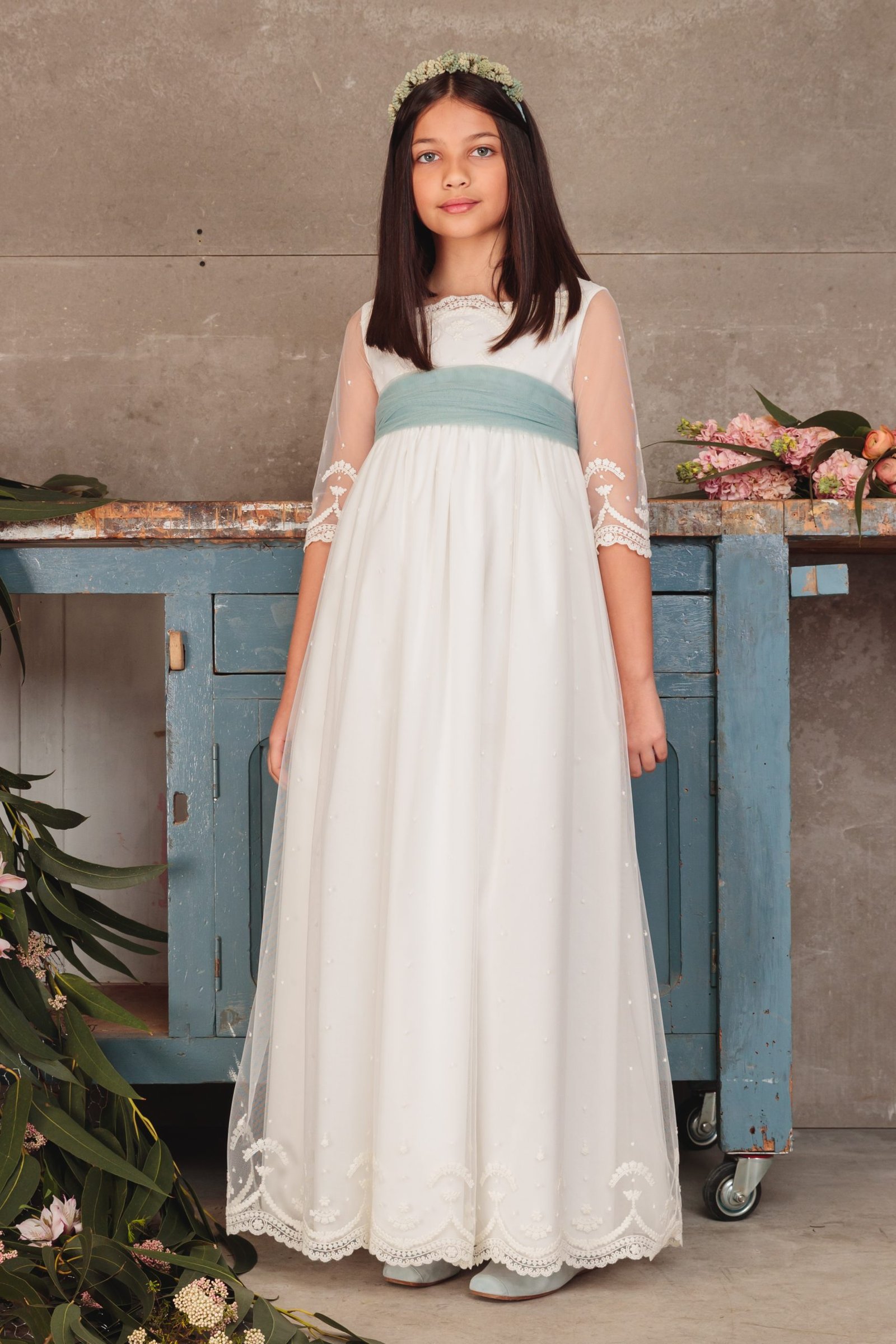 Vestido de comunión niña 2025 blanco con fajín verde agua, mangas de tul bordado y corona de flores, exclusivo en MartaMolina.com